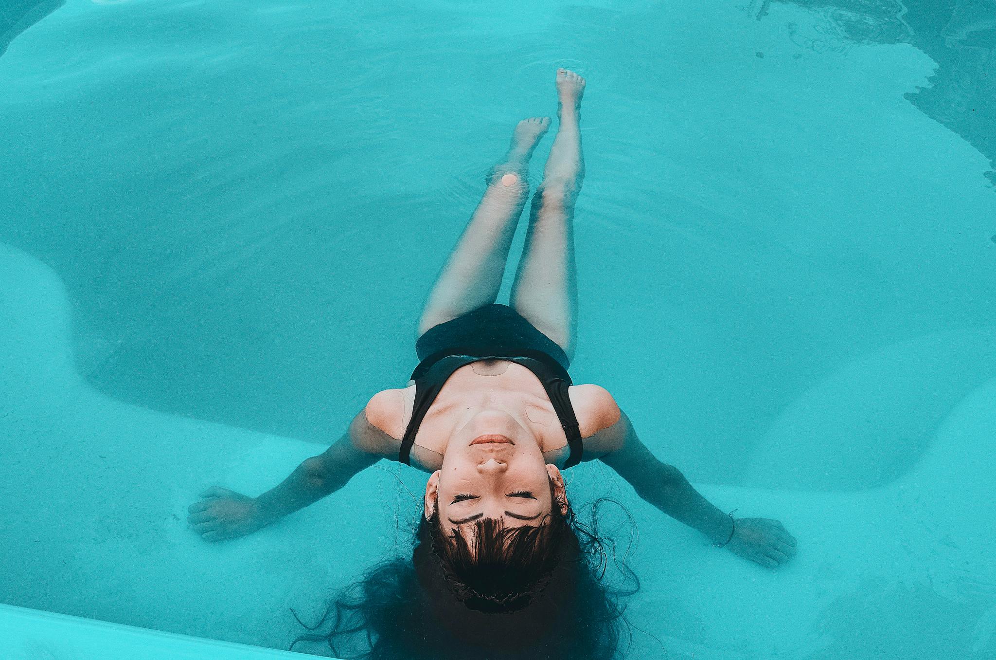 A woman in a black swimsuit floats gracefully in a serene swimming pool.